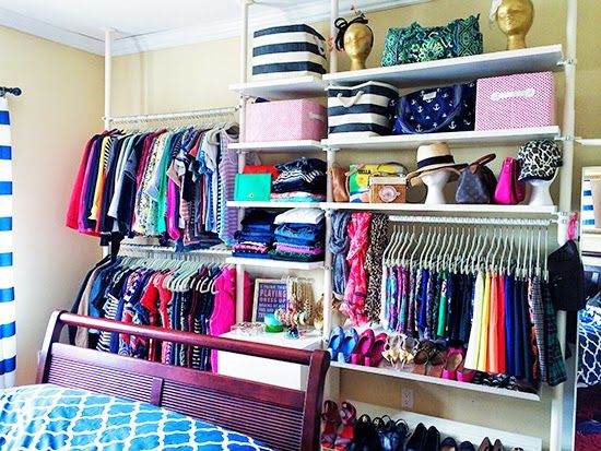 a wellorganized walkin closet is pictured. the closet is full of clothing, shoes, and accessories. the closet is arranged on a series of white shelves. the shelves are filled with boxes, bags, and hats. the clothing is hung on hangers and arranged by color. the shoes are neatly placed on the bottom shelves. in the foreground is a bed with blue and white linens and a dark wood frame. the closet is next to the bed and the rest of the closet can be seen behind it. the walls are painted a light yellow color. the closet appears neat and visually appealing.
