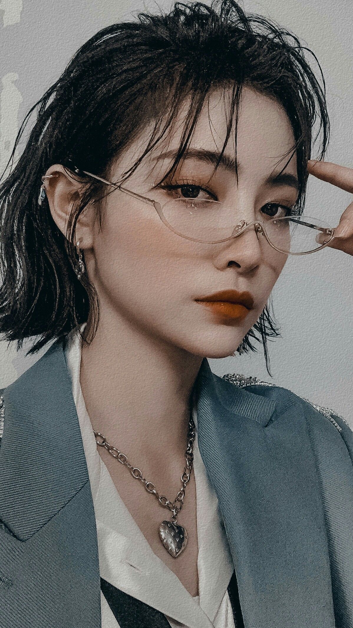 loseup portrait of a young asian woman with short, dark hair. she's wearing clear, cateye shaped glasses, a silver heartshaped necklace, and a stylish teal blazer. her expression is calm and serene, and the overall aesthetic is elegant and sophisticated. the background is a muted gray, which draws attention to the woman and her details.  the lighting is soft and diffused.