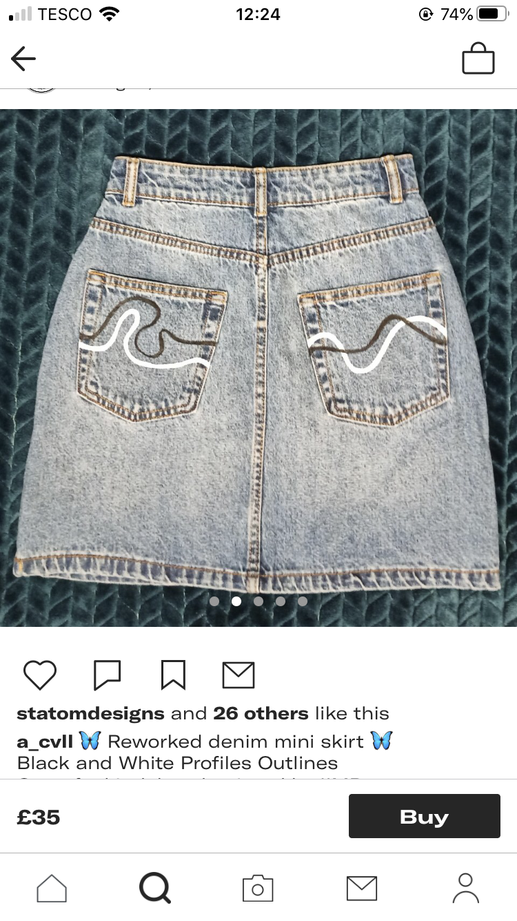 a picture of a denim skirt with black and white abstract detail on the back pockets. the picture is on a white background. at the bottom are social media icons for liking, commenting, sharing and sending. below that is a caption that says  "statomdesigns and 26 others like this a_cvll (blue butterfly emoji) reworked denim mini skirt (blue butterfly emoji) black and white profiles outlines"  at the very bottom is a button that says "buy" and the price £35.  the top of the image shows it was taken on a phone as it has the phone network "tesco" the time, and battery life.