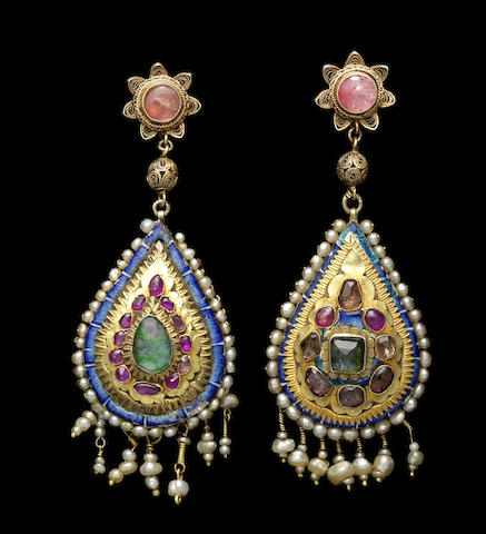 the image shows a pair of ornate, vintage earrings against a black background. the earrings are primarily gold, with teardrop shapes, adorned with gemstones including emeralds and rubies, as well as pearls. they feature intricate filigree detailing and blue enamel accents. the tops of the earrings have a flower design with a pink stone center, connected by a beaded section.
