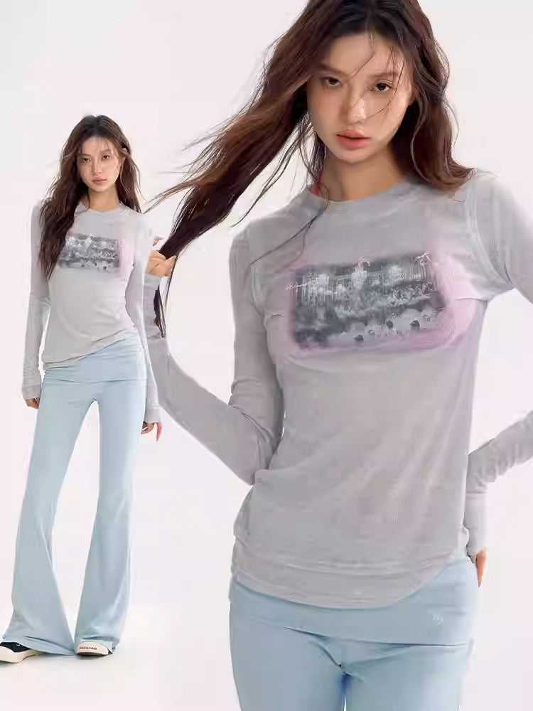 the image shows a woman modeling a stylish outfit. she is wearing a light grey longsleeved shirt with a graphic design and light blue pants. her hair is long and brown. she is posing in a studio setting. another woman wearing the same outfit is shown in the background. the overall look is casual, trendy, and elegant.