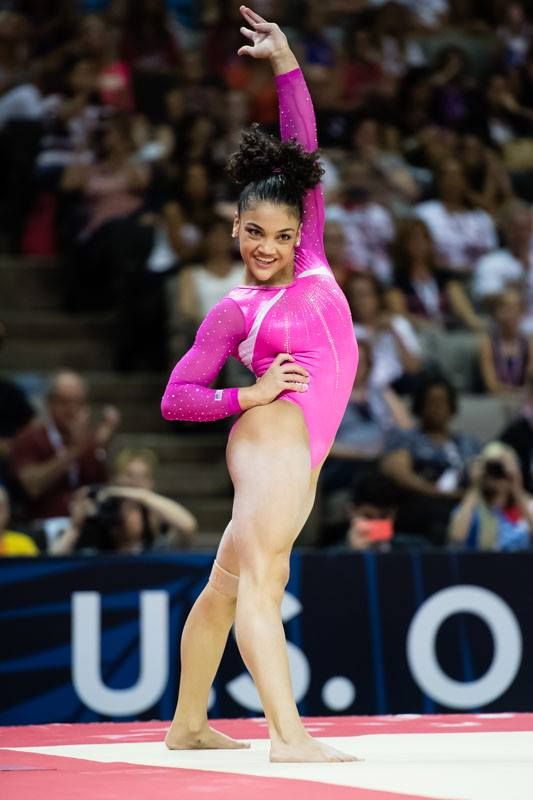 a female gymnast wearing a pink leotard performs a floor exercise routine in front of a cheering crowd. she has a big smile on her face and appears to be enjoying herself. her body is strong and flexible, and she is executing the move with grace and energy.