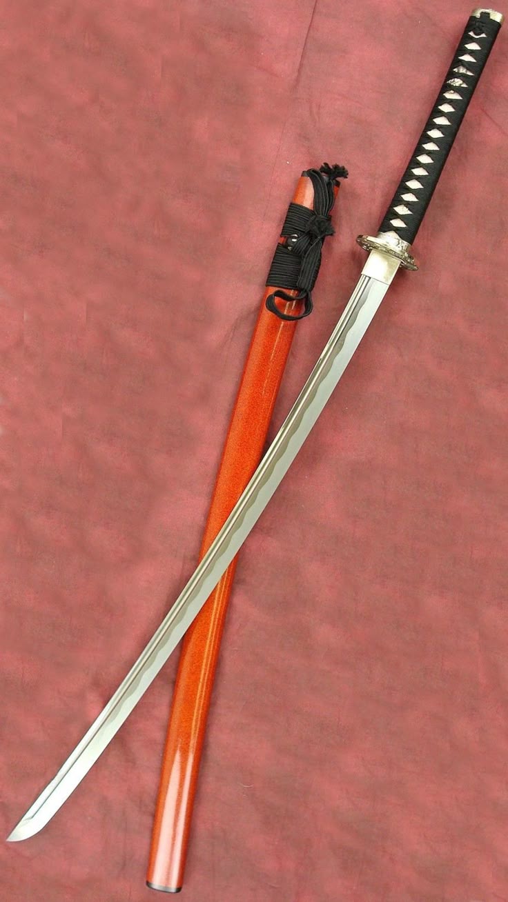 a katana sword with a black handle and a red scabbard is laying on a red surface. the sword is partially sheathed in its scabbard, revealing the blade. the tsuba (hand guard) is visible near the handle. the handle is black with white detailing, and the scabbard is a bright red color. the background is a plain red surface.
