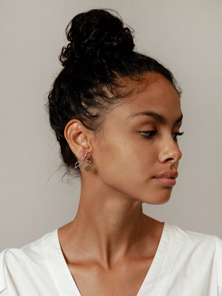 a portrait of a woman with her hair in a bun, wearing decorative earrings. she is facing to the right, showing her profile.