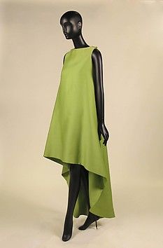a mannequin wearing a highlow, sleeveless green dress with a simple design. the dress is  sophisticated and stylish, giving it a vintage 1960s feel.  the mannequin is standing on a white background.