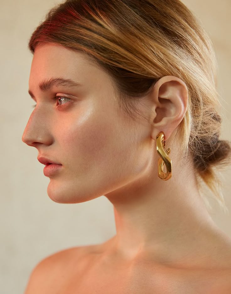 a profile portrait of a woman wearing gold twist earrings. her hair is pulled back in a bun.