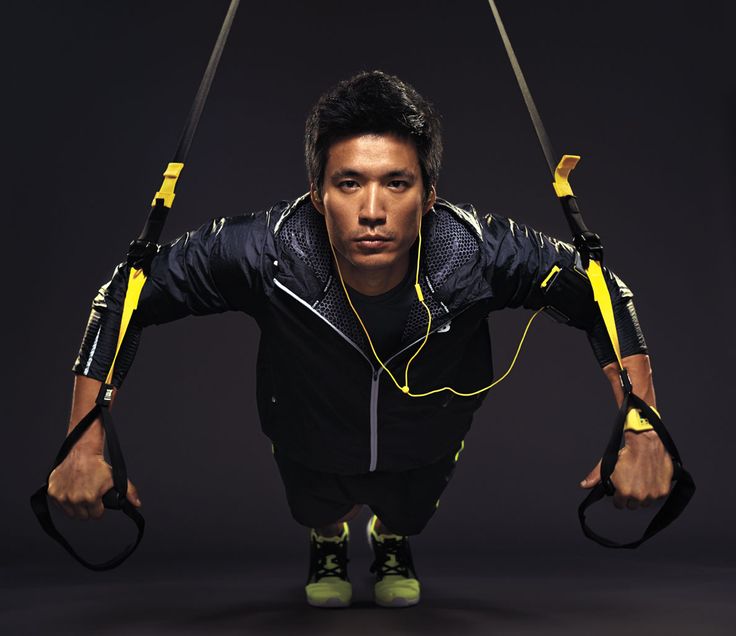 a fit man in a black jacket performs a pushup using a trx suspension trainer. he is determined and focused, showcasing his commitment to fitness. the black and yellow color scheme of his clothing and the equipment adds a visually dynamic element to the image.