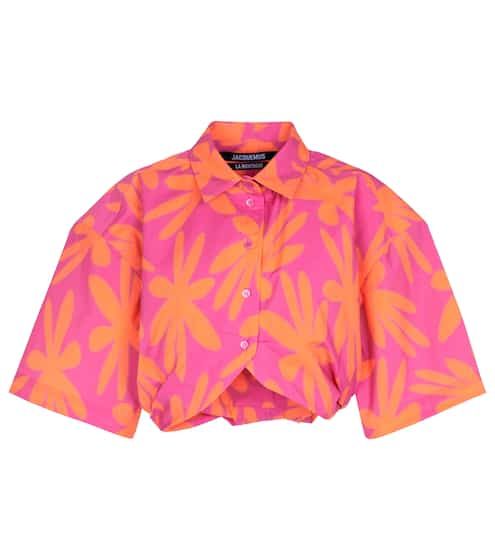 a shortsleeved buttondown shirt with a floral pattern. the shirt is pink with orange floral designs. it has a collar and is buttoned down the front. the brand label "jacquemus" is visible on the inside collar.