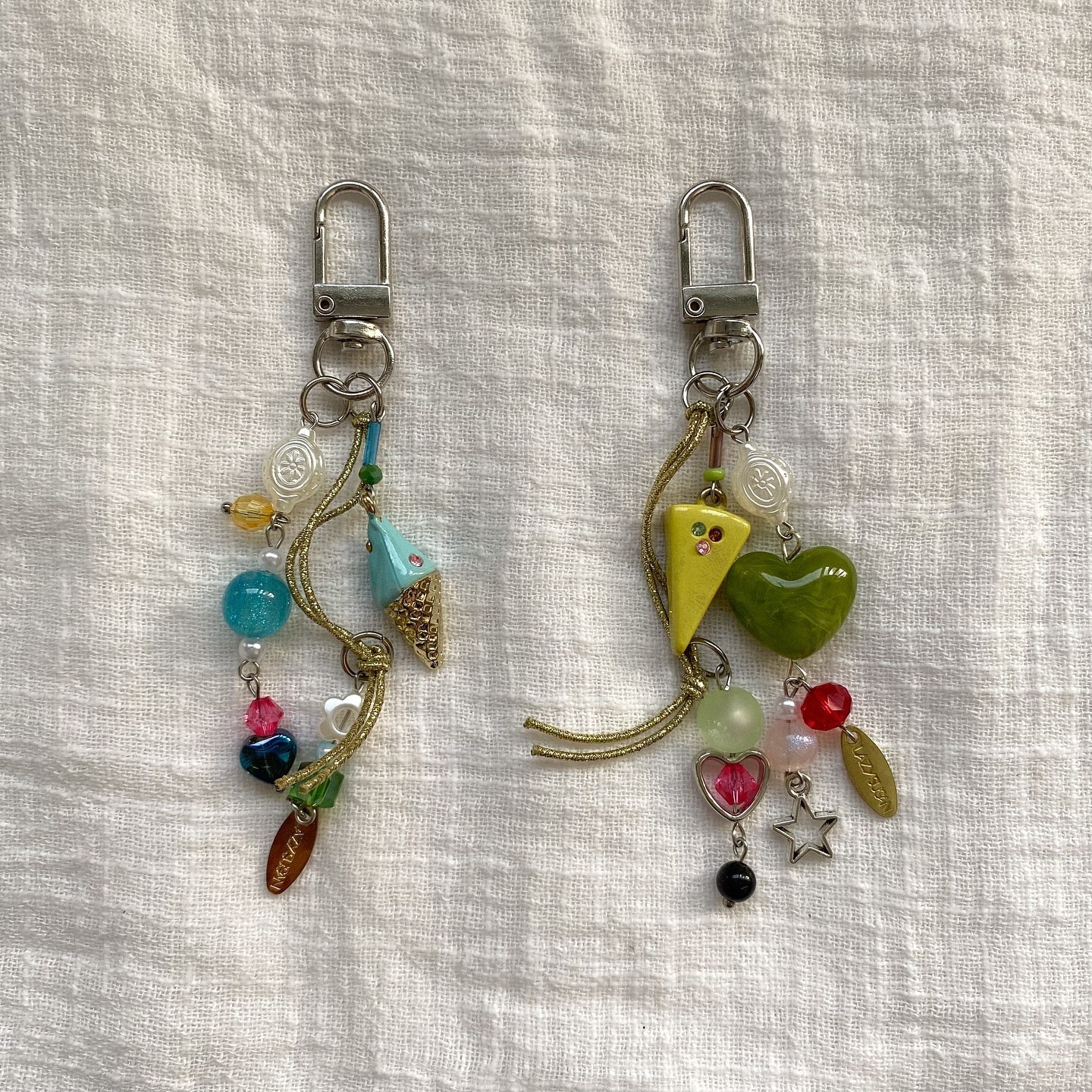 two keychains with lobster clasps are displayed on a white textured surface. each keychain is adorned with various charms and beads in a variety of colors and shapes, including ice cream cones, hearts, stars, and buttons.