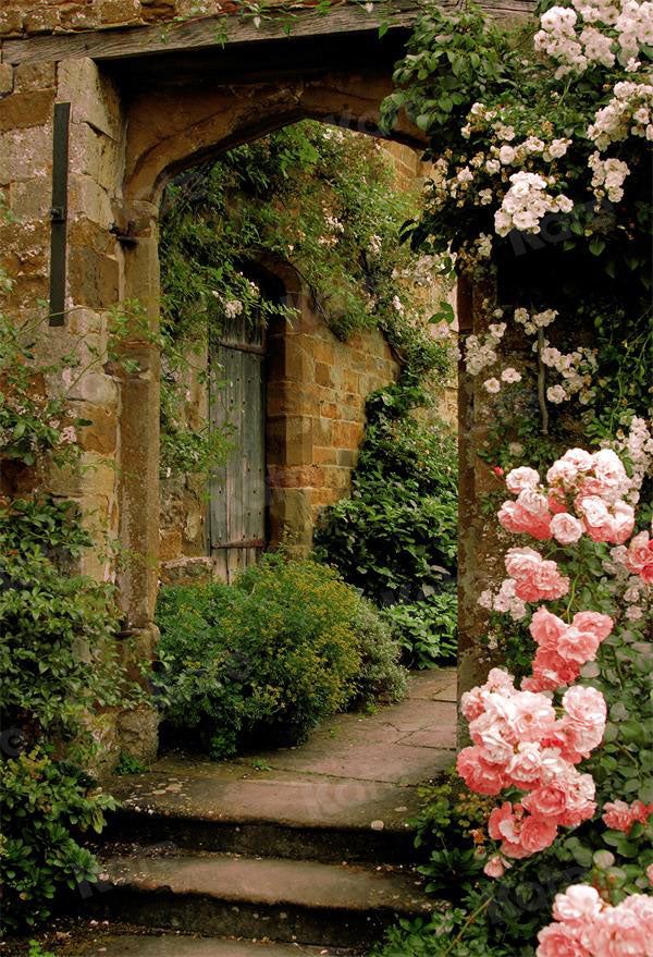 the image shows a stone archway leading into an overgrown garden. pink climbing roses are prominent on one side of the arch, and the archway itself is made of weathered stone. stone steps lead up to the archway, and a stone pathway continues into the garden. an old wooden door is visible through the archway. the garden is filled with greenery and flowers.