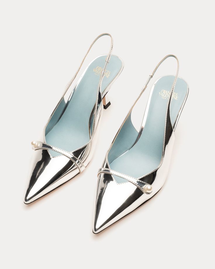 two silver pointedtoe slingback shoes with a pearl detail are arranged sidebyside on a light background. the shoes have a glossy, reflective finish and a light blue insole.
