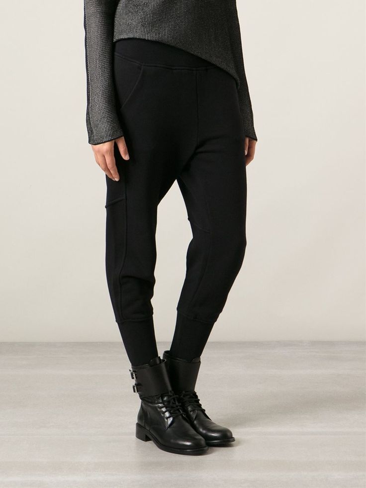 a woman stands in a grey longsleeved shirt and black drop crotch pants with black leather boots.