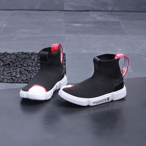 a pair of black sock sneakers with a white sole and red accents are displayed against a textured gray background. the sneakers are positioned slightly angled, showcasing their hightop design and trendy appeal. the studio lighting illuminates the shoes, highlighting their details and texture.
