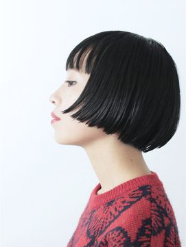 a woman with black straight hair cut into a bob with blunt bangs is shown in profile. the woman is wearing a red sweater and looking slightly down and to the left. she is shown against a white background.