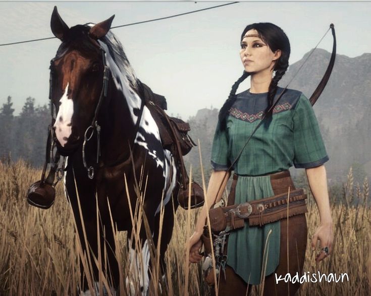 a female character from red dead redemption 2 standing in a field with a horse. she is wearing a green and black outfit and a leather belt with a holster. she is also wearing a headband and has her hair in braids. she is holding a bow and arrow. the horse is brown and white. the background is a field of grass.