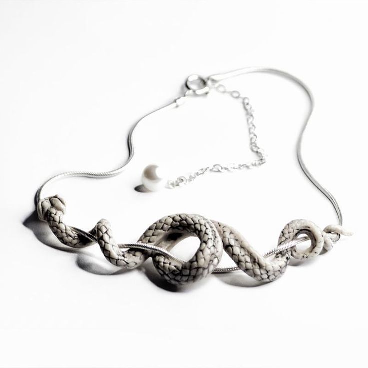 the image shows a necklace featuring a snake design coiled around a silver chain. the snake is textured and has a scaly appearance. a small pearllike bead hangs near the chain, and the necklace is secured with a clasp and an adjustable chain extension. the necklace is displayed against a white background.