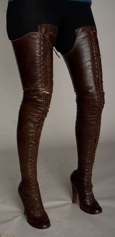 a woman is wearing a pair of brown leather thighhigh boots. the boots have a laceup front and a high heel. the woman is standing with her legs slightly apart, and her feet are pointed slightly outward. the image is lit from the front and slightly above, creating a soft shadow behind the woman. the background is a neutral gray.