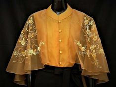 a closeup image showcasing a woman wearing a stunning goldtoned sheer top. this elegant piece, possibly a filipiniana "terno" blouse,  boasts intricate floral embroidery that adds a touch of luxury and tradition. the image is taken indoors with studio lighting, providing a clear and detailed view of the garment's exquisite craftsmanship.