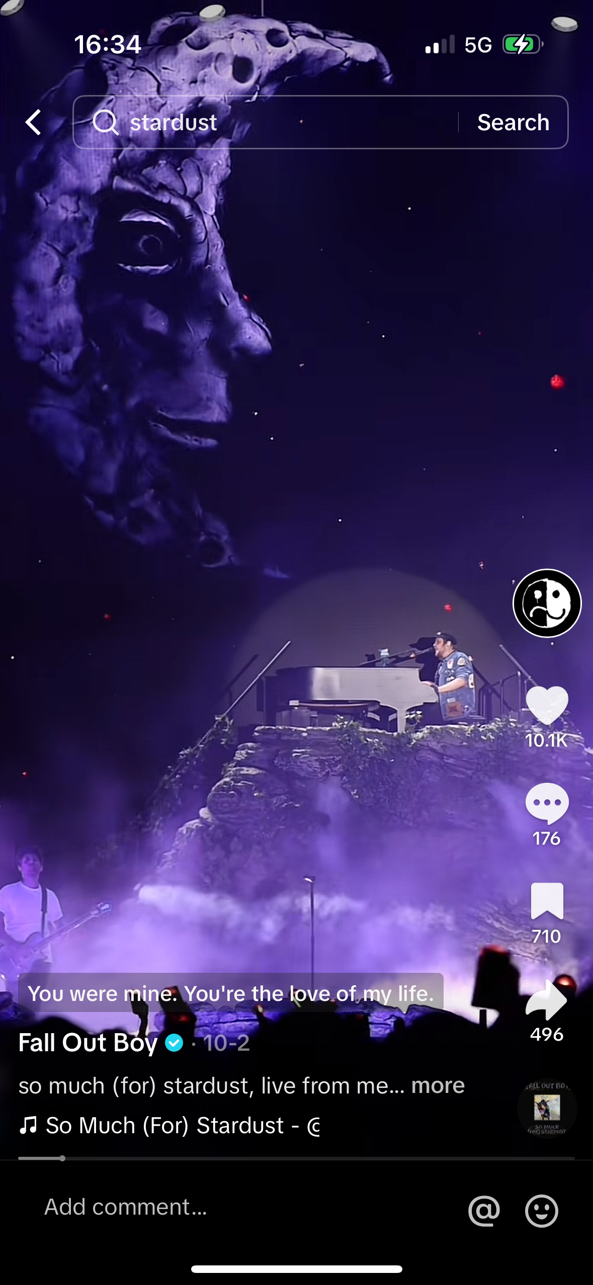 a screenshot of a fall out boy music video that is being streamed on a phone. the video is of the band performing live and the phone screen is also showing the comments that are being posted by fans. the video is titled "so much (for) stardust" and the screen also displays a comment that says, "you were mine, you're the love of my life." the phone screen also displays a number of different social media icons and buttons.