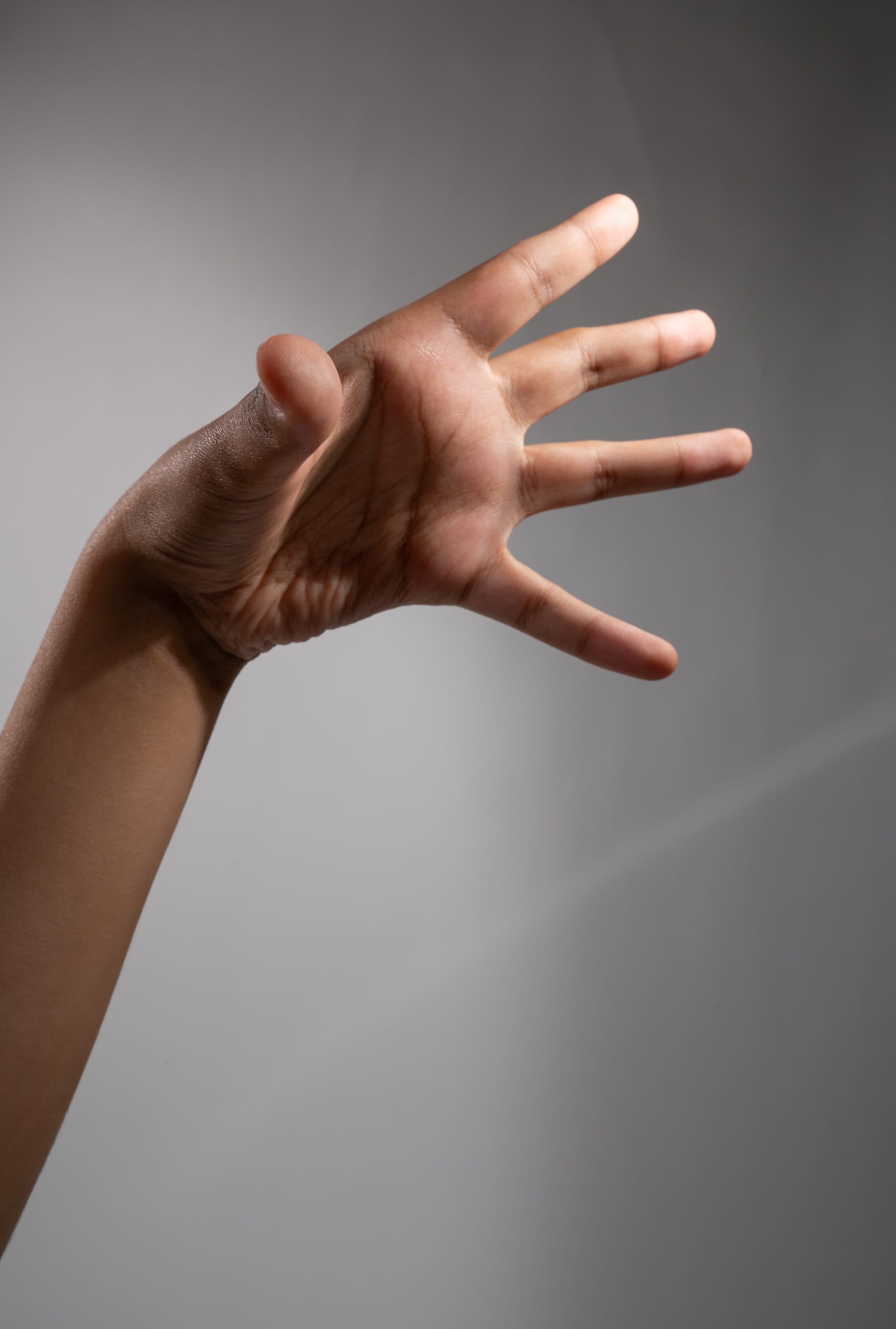 a closeup image of a hand and arm extended towards the viewer against a gray background. the image emphasizes the details of the skin and the position of the fingers. the studio lighting creates a soft, even illumination on the subject.