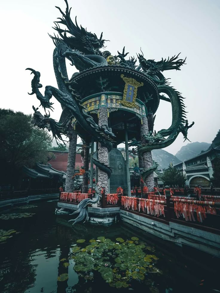 a detailed view of a dragonadorned temple structure in a pond with lily pads, set against a backdrop of other traditional buildings and a mountain range.