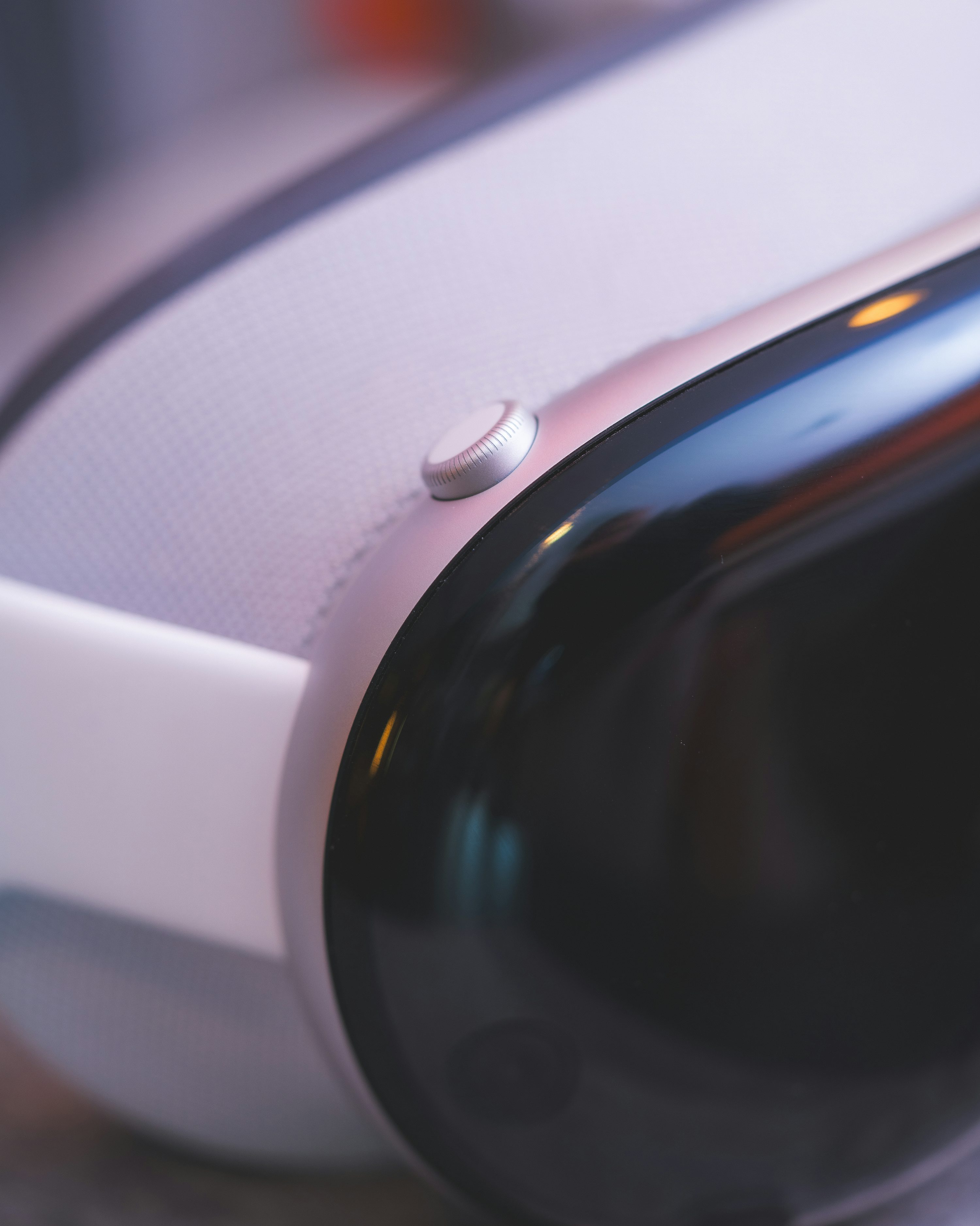 a closeup shot of a vr headset. the headset is mostly white and black, with a silver button on the side. the lens part is black and shiny. the headset's head padding is white and covered with mesh.