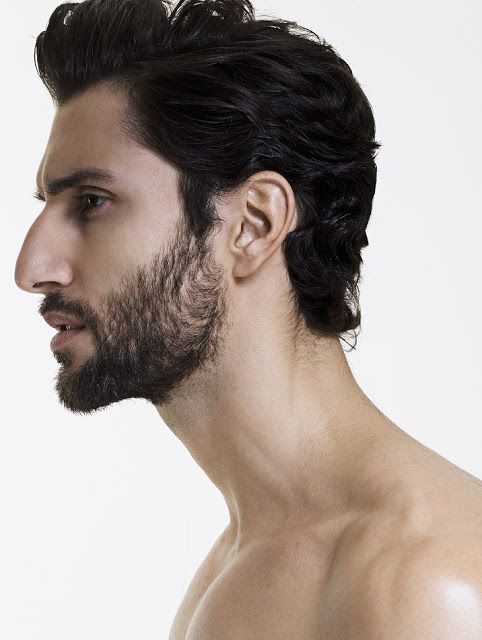 a profile headshot of a man with dark hair and a beard, facing left, with his bare chest and shoulders visible. he has a strong jawline and a distinctive nose. the background is plain white.