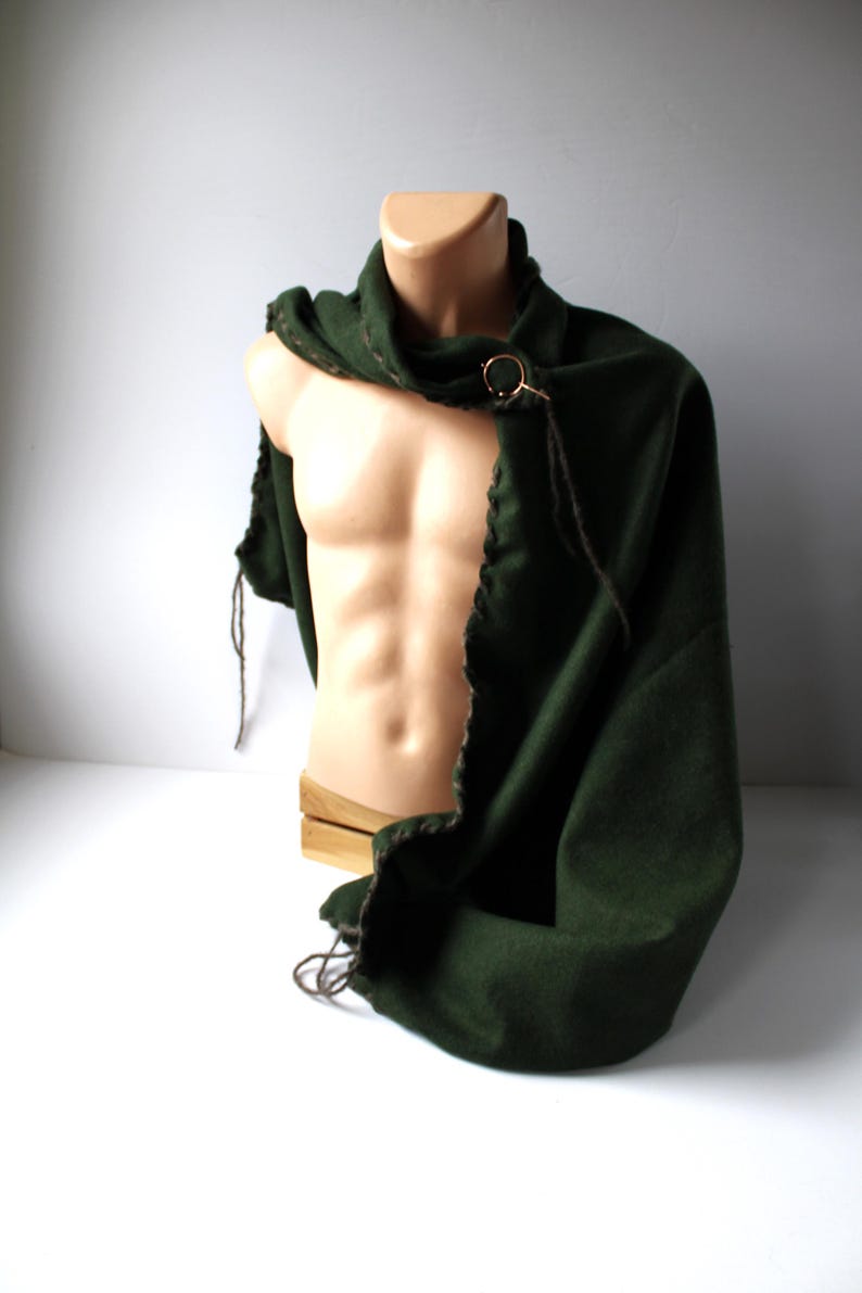 a dark green wool cape is draped on a mannequin and held in place by a round coppercolored brooch.