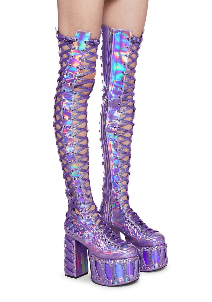 a pair of iridescent purple thighhigh platform boots with laceup details. the boots have a chunky platform sole and are made of a holographic material that shifts color in different lights. the boots are shown on a model's legs against a white background.