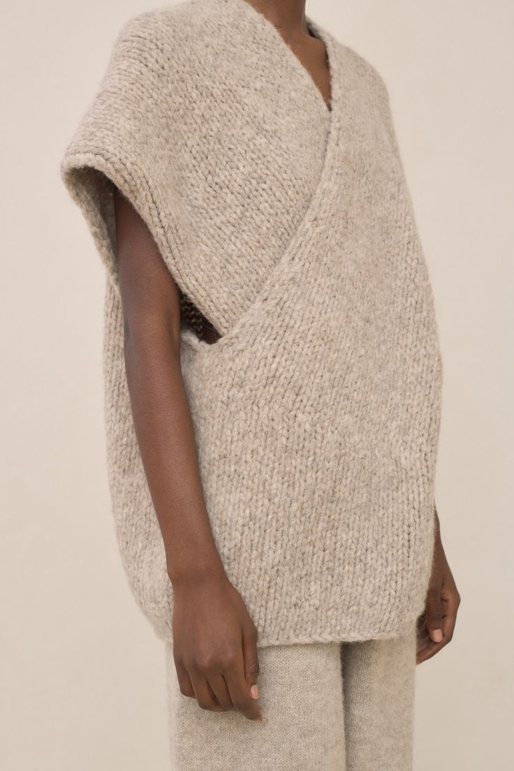 a woman wearing a cozy and stylish lightbrown knitted wrap vest. the outfit is minimalist and modern, perfect for a casual fall or winter look. the fabric seems soft and comfortable.