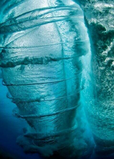 an underwater view of a wave forming a spiral shape. the water is clear and translucent, with shades of blue and aqua. the wave curls and twists, creating a dynamic and powerful scene.