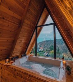 the image shows a luxurious jacuzzi tub nestled in the corner of a cozy aframe cabin. the tub is filled with bubbling water and surrounded by wooden walls and ceilings. large windows offer a stunning view of a mountainous landscape, bringing the beauty of nature indoors. candles and plants add to the relaxing ambiance. the overall scene evokes a feeling of peace and tranquility, ideal for a romantic getaway or a relaxing vacation.