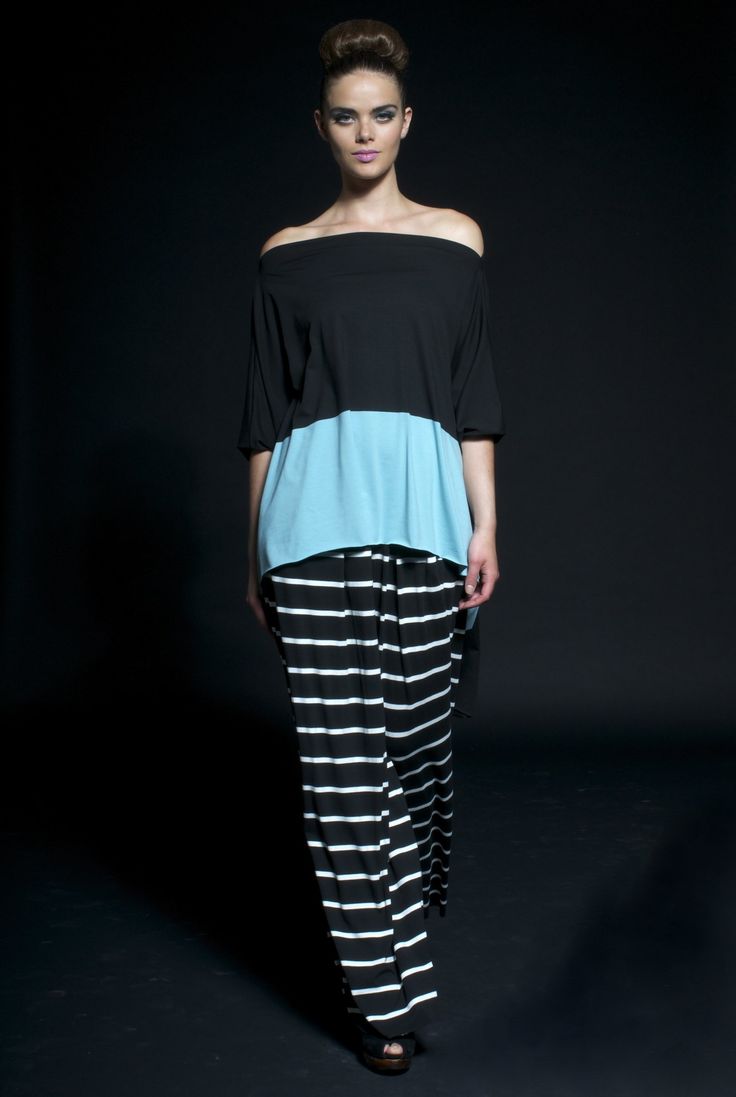 a woman in a black and white striped pants and a black and light blue top stands in a studio with a black background, looking at the camera with a casual elegant style.