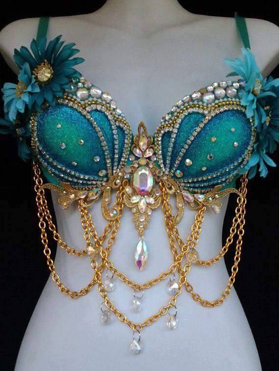 a teal beaded bra is shown on a white mannequin. the bra is adorned with flowers at the top, gold chains with clear rhinestones hanging from the center, and various shapes of beads, gems, and rhinestones covering the bust.