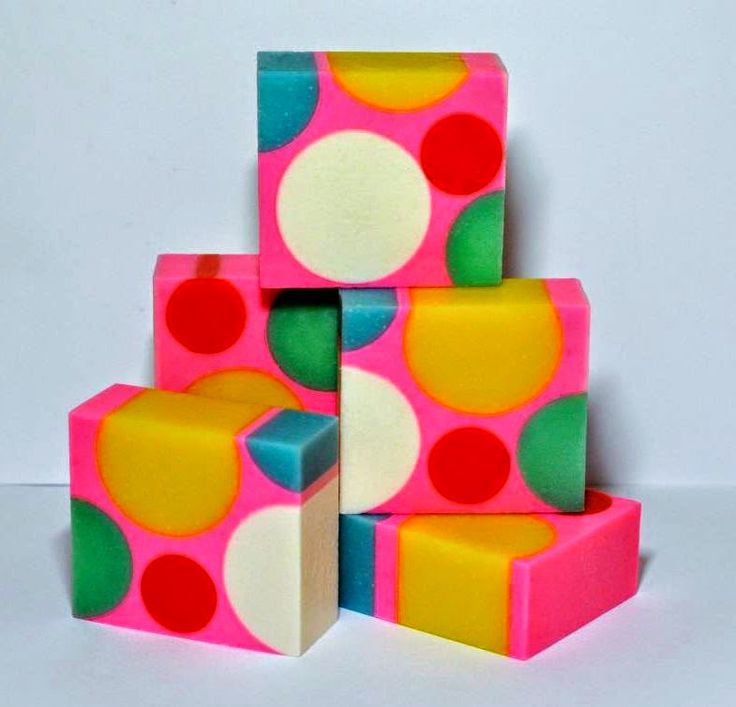 a stack of four colorful handmade soaps. each soap features a polka dot pattern of various colors on a pink base. the colors featured are pink, yellow, red, green, and white. the soap is handmade and stacked neatly on a white background.  the soaps are all geometric in shape.