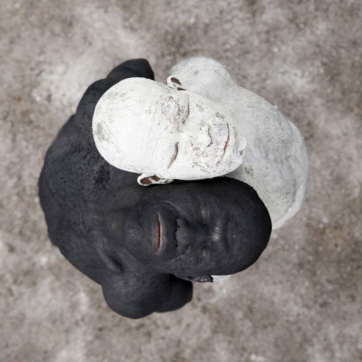 a black and white sculpture of two human figures, one black and one white, facing each other and embracing. the figures are lying on their sides, with their heads touching. the sculpture is a powerful statement about the beauty of diversity and the importance of unity.
