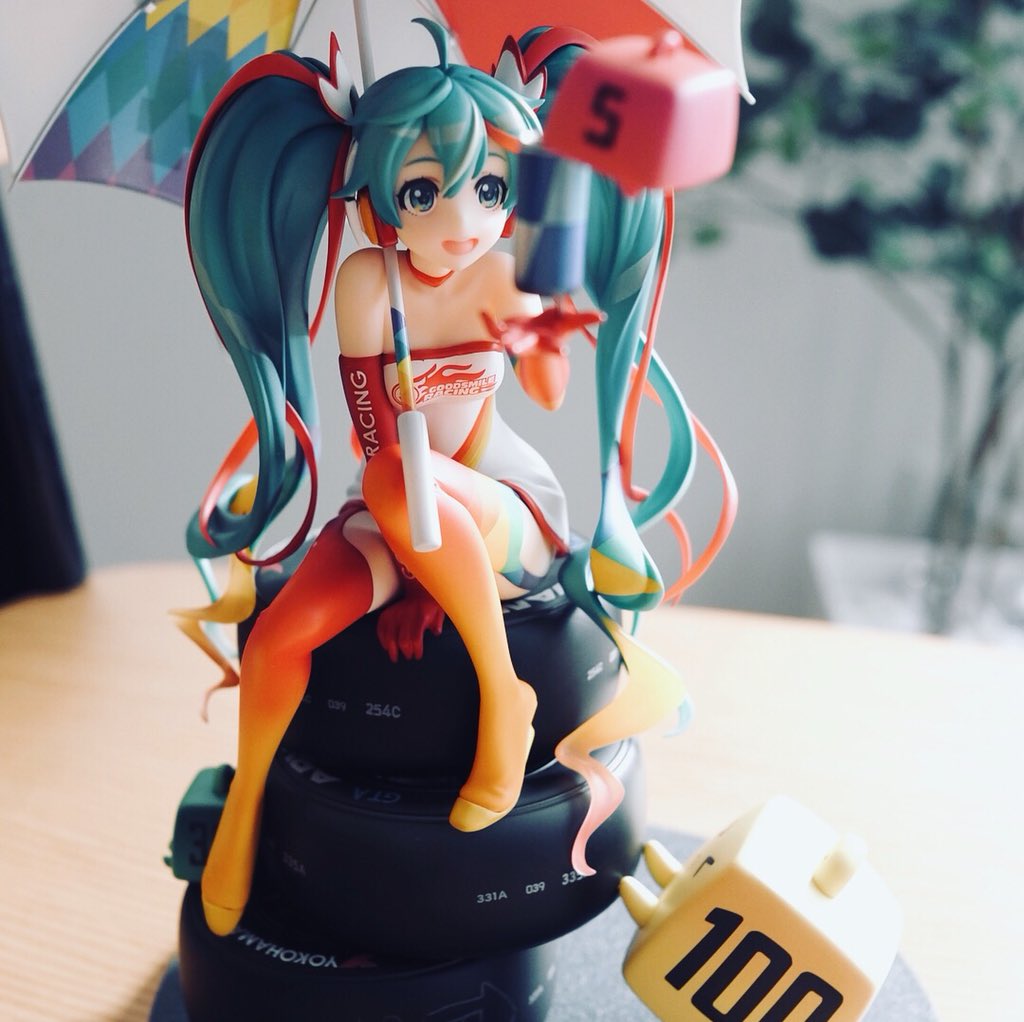 this is an image of a hatsune miku figurine. she is dressed in a racing outfit and holding a checkered flag umbrella. the figurine is very detailed and wellmade. the colors are bright and vibrant. the background is blurred, which helps to focus attention on the figurine.