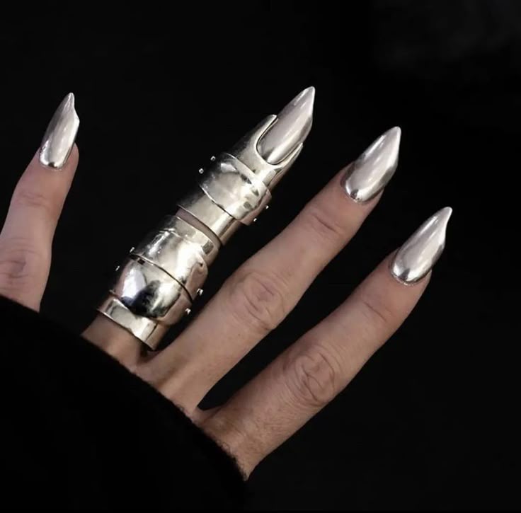 a closeup image of a hand with silver, pointed nails. one finger is adorned with a multisegmented, articulated silver ring that extends to the tip of the finger. the background is black, highlighting the reflective nature of the metal.