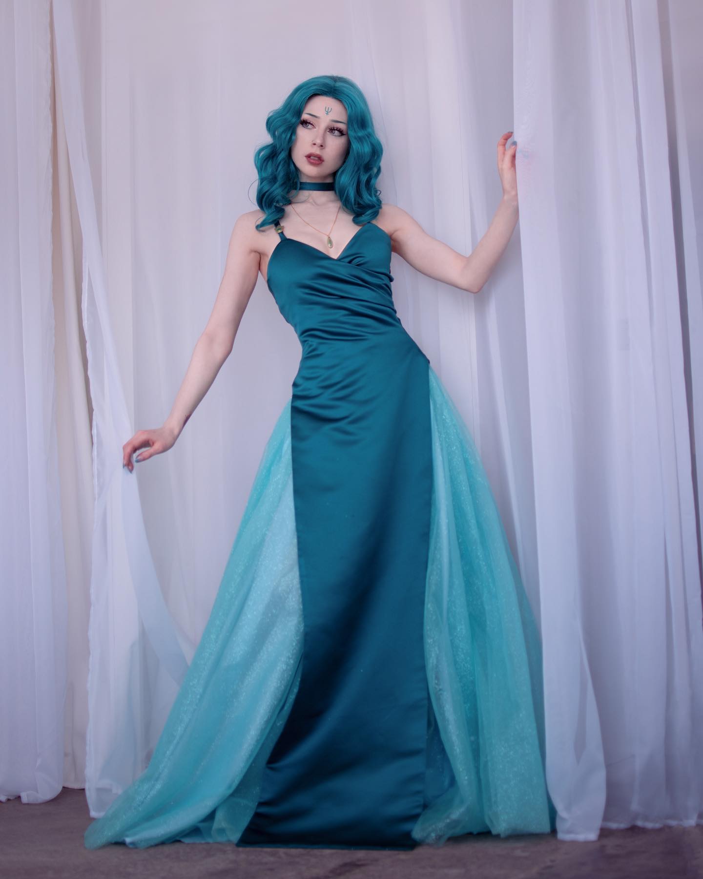 a fulllength shot of a young woman wearing a stunning teal and turquoise gown.  the dress is a combination of a teal satin bodice and skirt, overlaid with a flowing light turquoise tulle skirt.  the woman has vibrant teal hair, styled in loose waves, and she's wearing delicate jewelry, including a choker necklace. she is posing against a backdrop of white curtains. the overall aesthetic is elegant, ethereal, and slightly mystical.