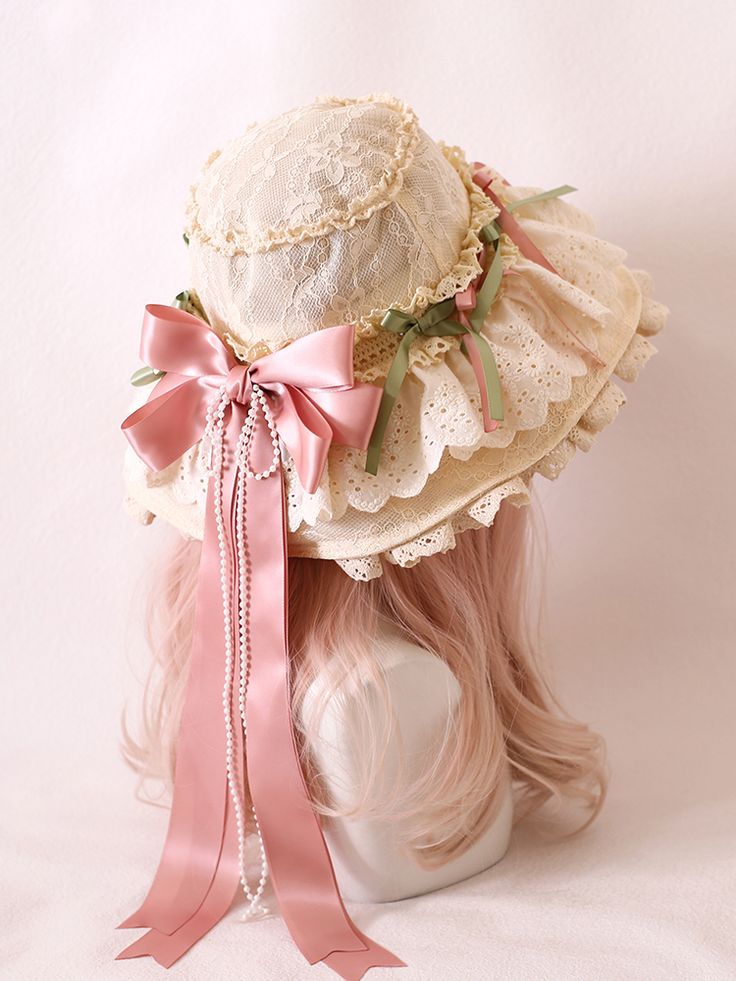 a back view of a cream lace bonnet styled in the lolita fashion. the bonnet is decorated with pink and green ribbon, a large pink bow, and strings of pearls.