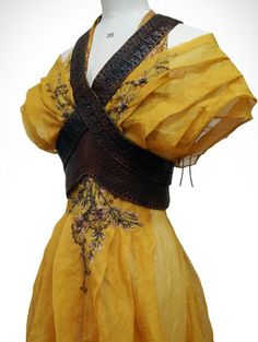 the image showcases a stunning yellow gown with intricate embroidery and a brown leather bodice. the dress, likely a costume, evokes a sense of historical or fantasy fashion, perhaps inspired by medieval or renaissance styles. the soft, flowing fabric and detailed embellishments suggest a garment designed for a theatrical or ceremonial purpose.