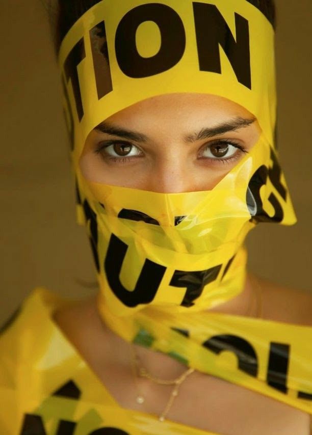a portrait of a woman with caution tape over her face,  she has a serious expression and  her eyes are visible. the yellow caution tape is a striking contrast to her dark hair and skin.