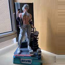 the image shows a meticulously detailed figurine of gojo satoru from the anime series jujutsu kaisen.  the figure depicts gojo in a casual pose, seemingly holding a smartphone while dressed in gym attire. he's muscular and has his characteristic white hair.  the figure is positioned on a base that includes weightlifting equipment like dumbbells, suggesting a gym theme. the overall setting appears to be an indoor display, possibly a home or collector's showcase. the figurine is highquality and appears to be a professionally produced collectible.