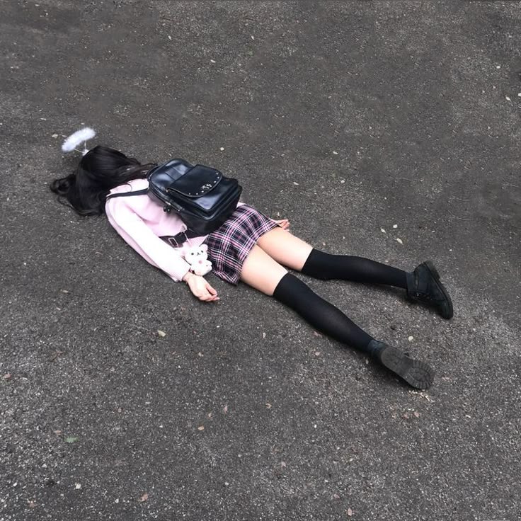 a girl wearing a school uniform lies face down on the ground with a backpack and a teddy bear, and an angel halo around her head.