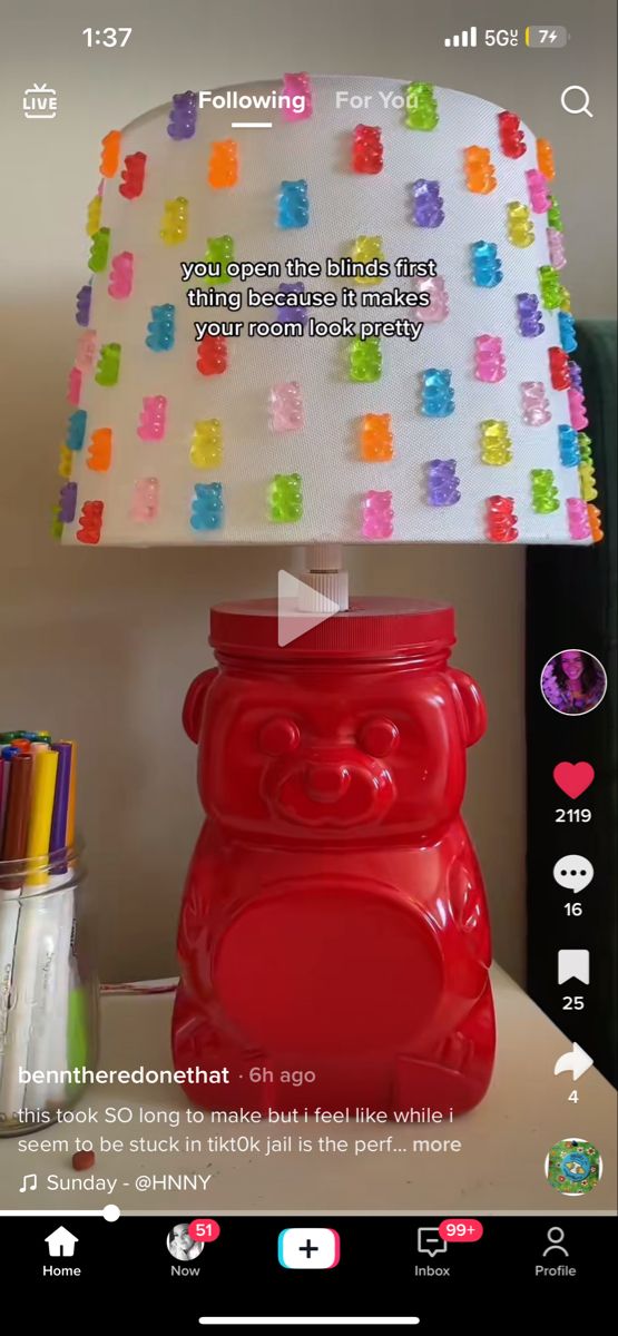 a red bear lamp with a white lampshade decorated with gummy bears. the image was taken from a phone screen, showing a video with the user's caption. the video is about the user's home decor.