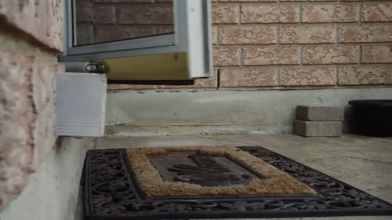 this is an image of a front door. there is a doorstop behind the door to keep it open. there is a welcome mat in front of the door. the house is made of brick.