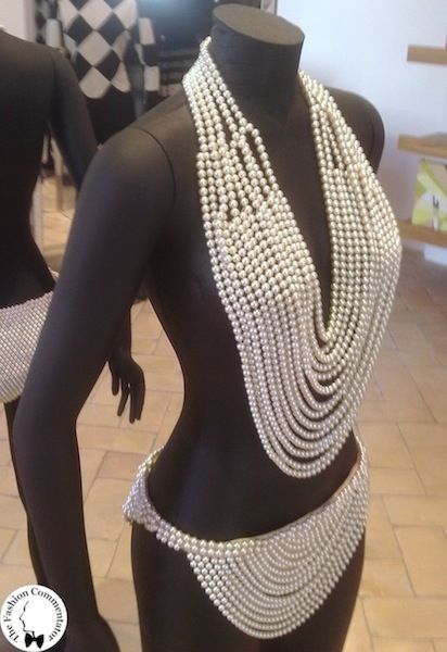 a darkskinned mannequin displays a swimsuit made entirely of pearls. the top is a halterstyle necklace that cascades down the torso in multiple strands, while the bottom is a bikini brief made of clustered pearls.