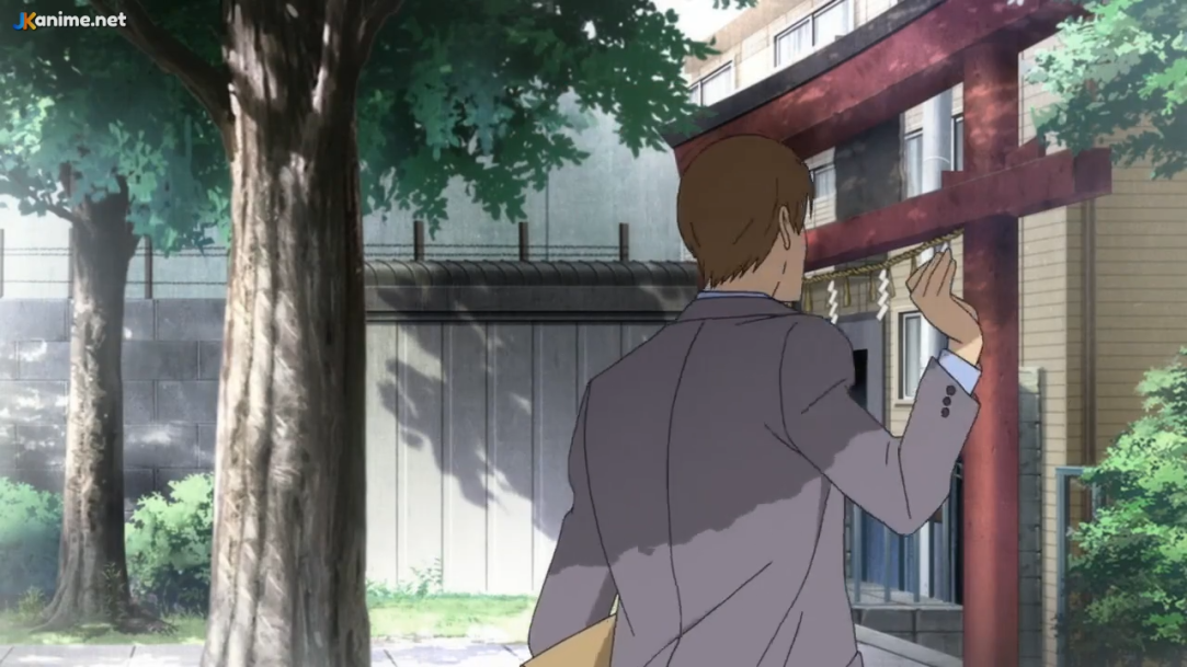 this anime screenshot shows a man from the back, waving goodbye while holding a brown folder. he is standing in front of a building with a red torii gate. there are green trees to the side. the overall lighting suggests a bright sunny day.
