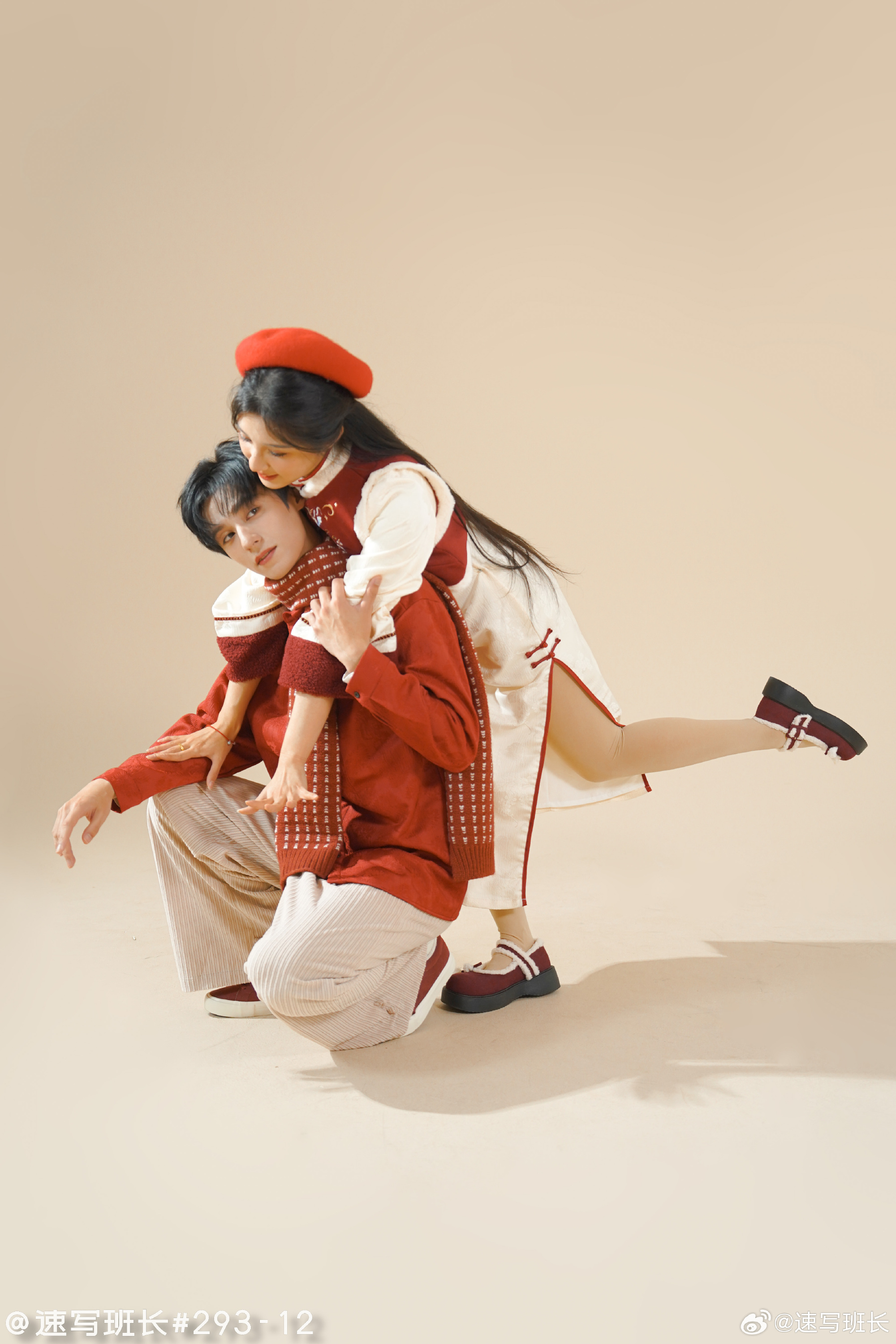 a man and a woman are posing for a photo. the woman is wearing a red dress and a red beret. she is leaning on the man's back. the man is wearing a red jacket, white pants, and a red scarf. they are both wearing black shoes. the background is a light beige color.