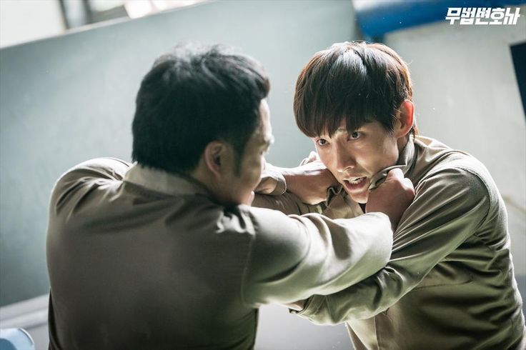 two men are engaged in a closeup fight, their faces contorted in concentration and anger as they grapple for control. the action is intense and real, highlighting the seriousness of the situation. the men are wearing prison uniforms, adding to the dramatic context of the scene. the image is a powerful depiction of human conflict and aggression, likely from a korean drama.